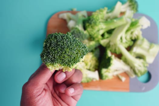 Broccoli floret is held above a wooden cutting board with more broccoli.