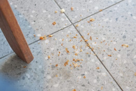 Small crumbs are spread across the floor under a chair in a well-lit space.