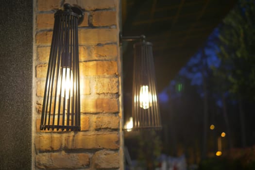 Warm light from rustic lamps highlights the brick wall in the evening.