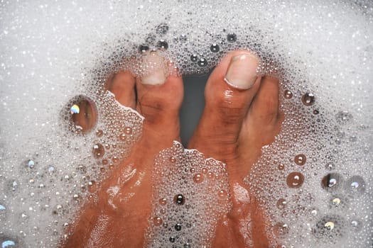 A pair of feet resting in a bubble-filled bath enjoying relaxation.