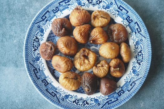 Dried figs displayed neatly on a blue patterned plate in bright light.