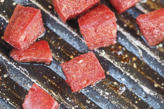 Beef cubes are placed on a grill cooking surface for preparation.