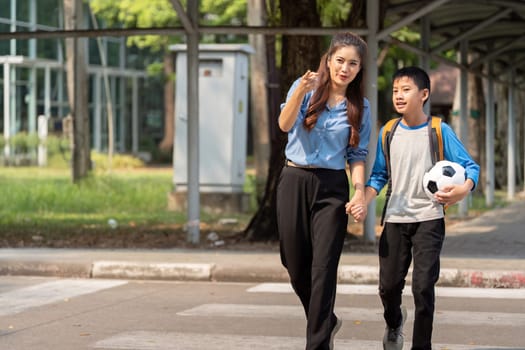 A happy moment as a mother holds her son hand, both excited for the school day ahead, with a soccer ball by their side.