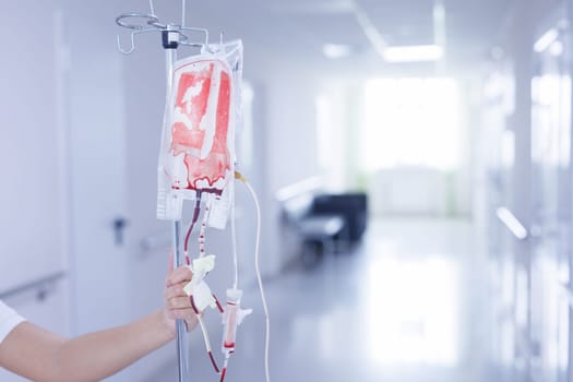 Blood transfusion bag on IV stand held by a medical professional in bright hospital corridor, emergency care setup.