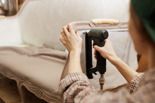 Close-up of woman upholstering vintage sofa with pneumatic stapler, focusing on craftsmanship and detail.