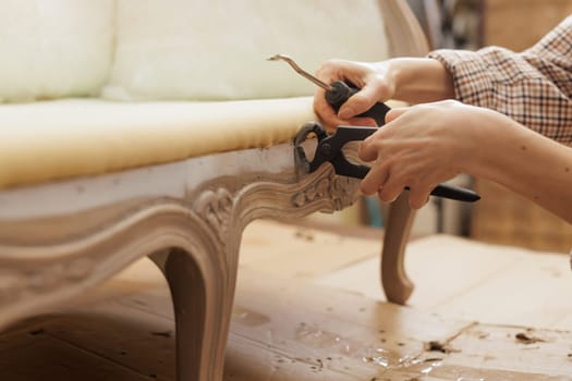 Close-up of hands using pliers and a screwdriver to remove old staples from vintage furniture during reupholstery.