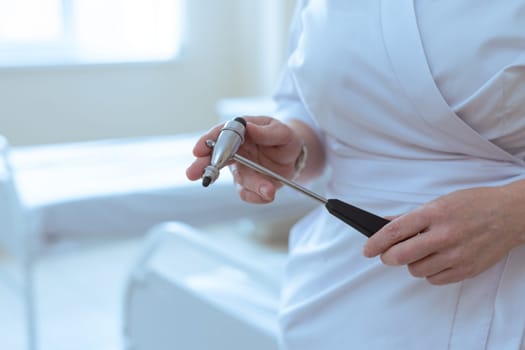 Doctor holding a reflex hammer in a medical room, preparing for neurological examination of a patient.