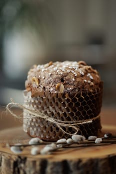 Artisan chocolate Easter cake with hazelnuts and sugar topping, wrapped in eco paper on rustic wood slab.