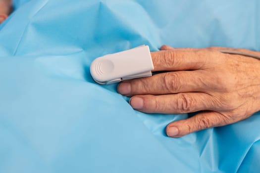 Close-up of senior patient's hand with pulse oximeter on finger, monitoring oxygen saturation in hospital care.