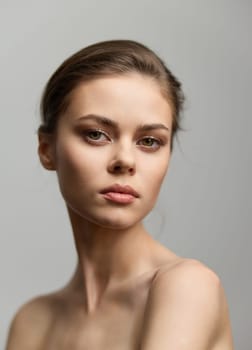Portrait of a serene young woman with a clean, natural look, showcasing her features against a subtle gray backdrop, capturing the essence of beauty and grace.