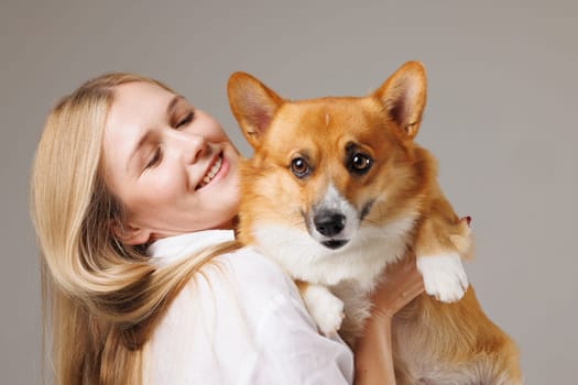 Joyful young woman holding her adorable Corgi dog, both looking happy and affectionate, in a close-up moment.