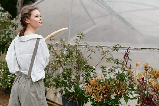 A young woman wearing casual overalls and a light shirt is tending to plants in a greenhouse The earthy color palette enhances her connection to gardening, evoking feelings of tranquility and harmony with nature