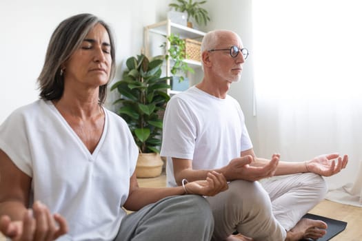 Mature caucasian couple meditating at home living room sitting on a mat. Lifestyle concept.