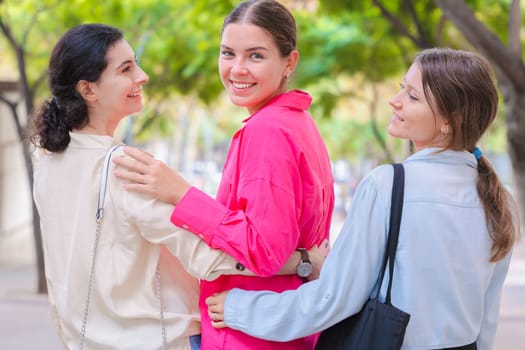 Three Caucasian women walk outdoors, smiling and enjoying a casual moment together. Their relaxed vibe, friendship, and cheerful energy are captured in a bright, tree-lined environment.
