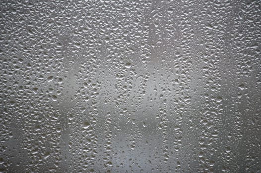 Close-up view of water condensation droplets forming patterns on a foggy glass window, creating a textured and abstract background illuminated by light for artistic and scientific purposes