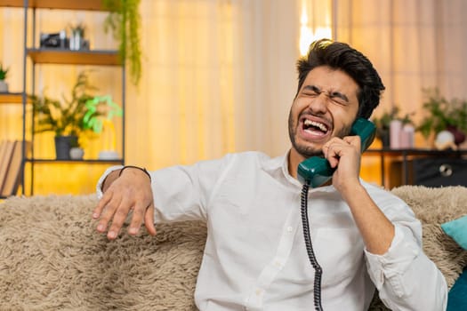 Indian man holding an old 90s vintage phone, speaking loudly through the speakerphone. Arabian guy face shows determination, confidence, having focused conversation, exuding strong, assertive presence