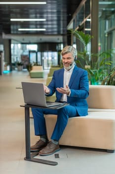Caucasian businessman wearing headset, call center or support service operator helpline, having talk with client or colleague communication support in office lobby. Guy in suit sits on couch in hotel.