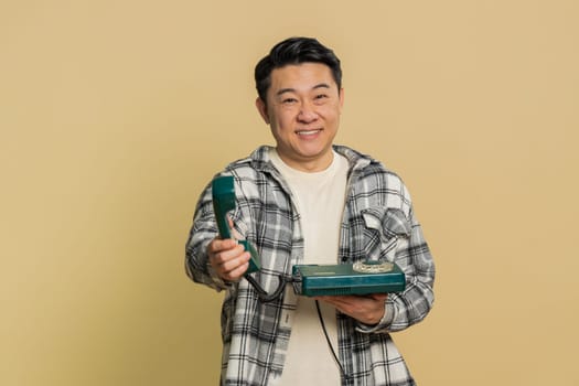 Hey you, call me back. Asian middle-aged man talking on wired landline vintage telephone of 80s advertising proposition of conversation, online shopping. Mature Chinese guy on beige background indoors