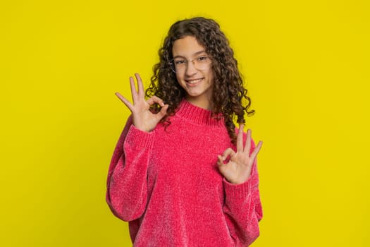 Okay. Happy Caucasian young teenager girl looking approvingly at camera showing ok gesture, like sign positive feedback, approve something good, celebrate victory. Teen child kid on yellow background