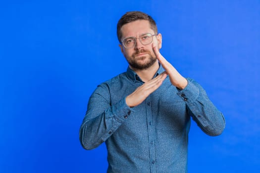 Tired serious upset Caucasian middle-aged man showing time out gesture, limit or stop sign, no pressure, I need more time, take a break, relax, rest, help. Young adult guy isolated on blue background
