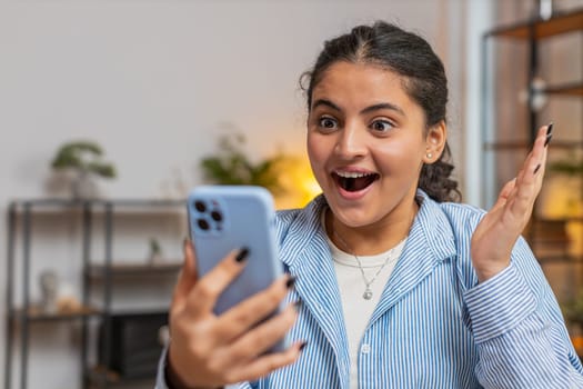 Oh my God Wow. Excited happy joyful winner Caucasian woman use smartphone typing browsing found great win good news celebrate victory. Girl with mobile phone at home office table workplace. Lifestyle.