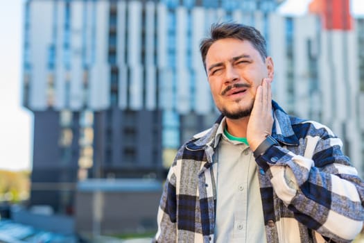 Mature Caucasian man tourist standing on downtown city street feeling toothache bad unpleasant symptoms, guy suffering from pain holding hand on cheek jaw damaged dental nerve needs medical help.