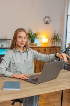 Caucasian businesswoman freelancer opens laptop and working on project while sitting at home office table. Adult woman girl works on netbook, sends messages, makes online purchases, watching movies.