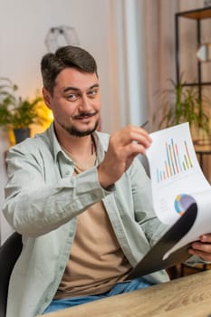 Caucasian freelancer accountant working with financial graph documents, calculate taxes for charts and reports at home office desk. Guy working on laptop computer, planning expenses budget. Vertical.