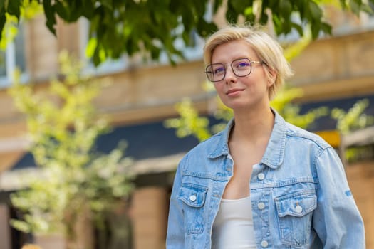 Caucasian woman tourist walking in urban city street background in summer daytime outdoors. Blonde girl traveler having positive good mood enjoying walking on urban city street. Town lifestyles.
