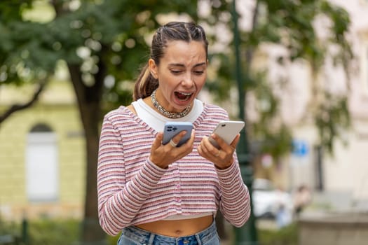 Irritated nervous stressed Caucasian young woman talking screaming on two mobile phones having conversation conflict quarrel complaint dispute discuss solve problem outdoors. Girl on urban city street