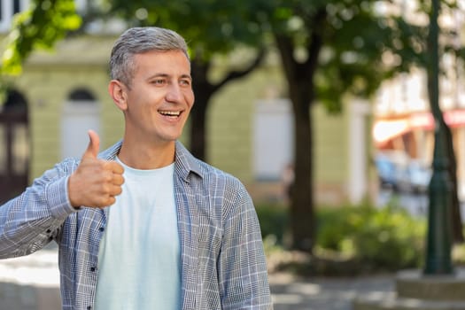 Like. Happy mature man raises thumbs up agrees with something gives positive reply recommends advertisement good idea feedback, celebrating success victory outdoors. Handsome guy on city street.