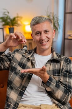 Happy Caucasian young man with gray hair real estate agent lifting hand showing the keys of new home house apartment, buying or renting property, mortgage loan investment at modern home room apartment