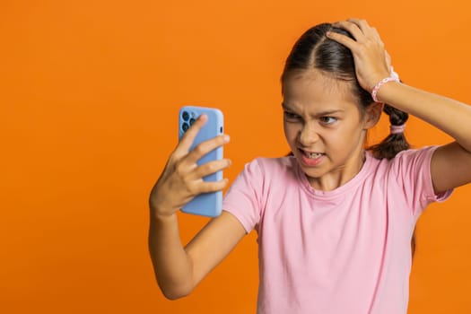 Upset sad preteen child girl kid use smartphone typing browsing, play game, loses, surprised by sudden lottery results, bad fortune, loss, fail, unlucky news. Sad children on orange background indoors