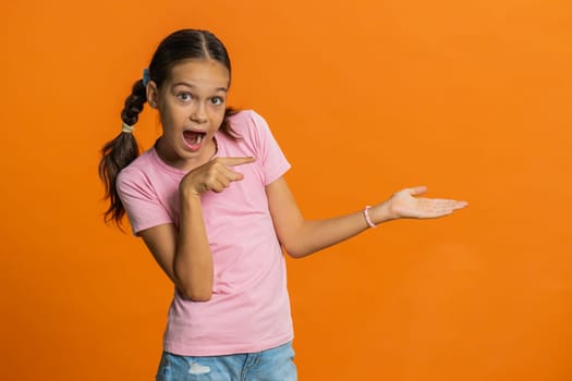 Preteen child girl kid showing thumbs up pointing right empty place, advertising area for commercial discount text, copy space for goods promotion advertisement. Teenager children on orange background