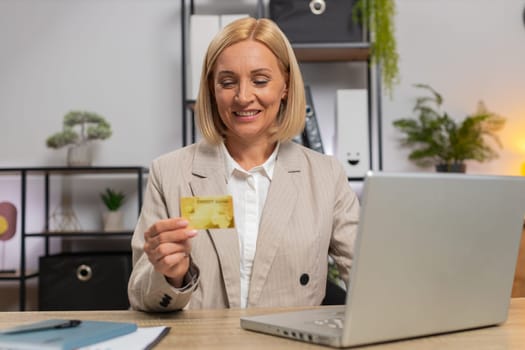 Happy Caucasian businesswoman using bank credit card and laptop for online shopping payments at home office. Business transaction. Smiling girl freelancer purchase with computer E-banking app service.