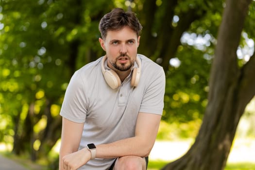 Headphones, smartwatch, fitness man in city park for running, training or marathon, cardio or morning routine. Exercise, app or runner with music, energy or workout, steps or heart rate progress.