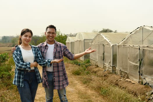 Proud farmers standing in front of their greenhouse farm. Sustainable cultivation concept.