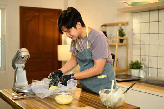 Young man in an apron preparing homemade butter in a modern kitchen.