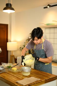 Man pouring freshly churned butter into strainer to separate buttermilk in a home kitchen.