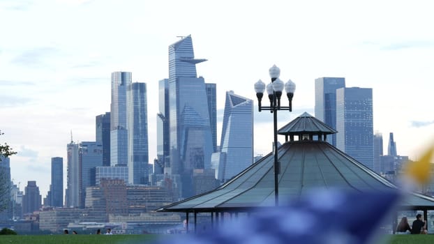 New York City, United States - 11 Sept 2023: Waterfront skyline, Manhattan Midtown Hudson Yards, riverfront skyscrapers. Waterside cityscape from Pier A Park, Hoboken, New Jersey. People on grass lawn