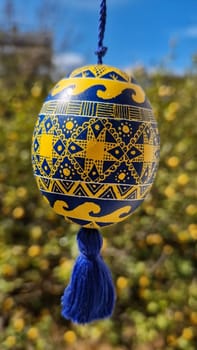Delicate traditional Ukrainian pysanka decorated in yellow and blue hangs from a string, showcasing intricate folk designs.