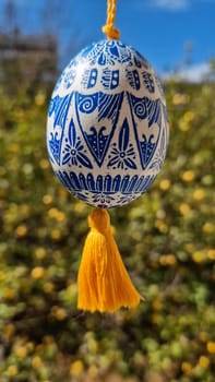 A stunning Ukrainian pysanka, showcasing traditional Easter egg designs, hangs against a backdrop of blooming flowers.