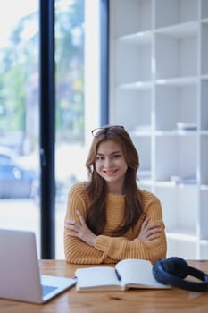 Smiling young woman engaged in online e-learning at her desk with a laptop notebook and headphones creating a positive study atmosphere for success.
