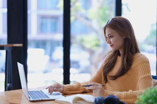 Smiling young woman engaged in online e-learning at her desk with a laptop notebook and headphones creating a positive study atmosphere for success.