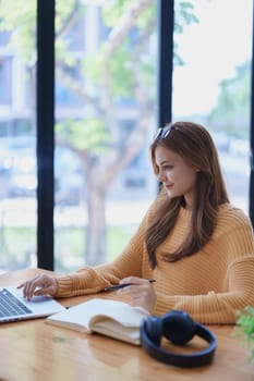 Smiling young woman engaged in online e-learning at her desk with a laptop notebook and headphones creating a positive study atmosphere for success.