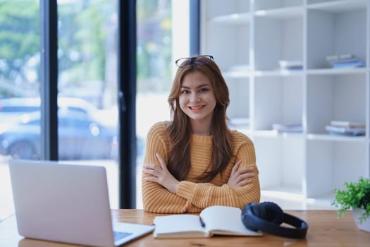 Smiling young woman engaged in online e-learning at her desk with a laptop notebook and headphones creating a positive study atmosphere for success.