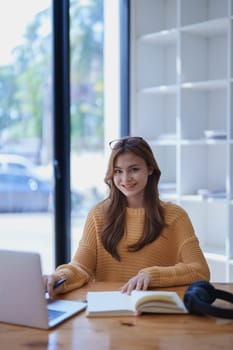 Smiling young woman engaged in online e-learning at her desk with a laptop notebook and headphones creating a positive study atmosphere for success.