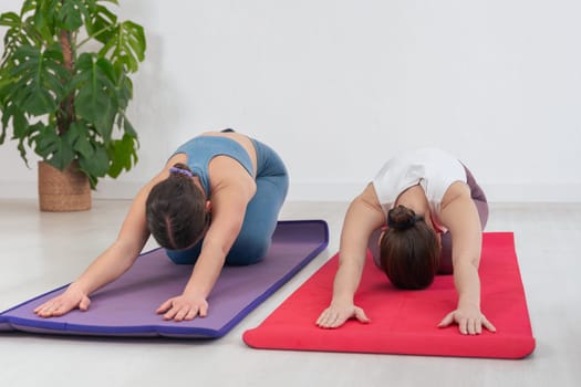 Caucasian women doing childs pose on yoga mats in a peaceful indoor space. Focused on relaxation, mindfulness, and flexibility with calm atmosphere and soft natural light around them