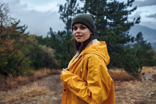 A woman in a yellow raincoat standing on a trail, surrounded by majestic mountains, ready for a hiking adventure