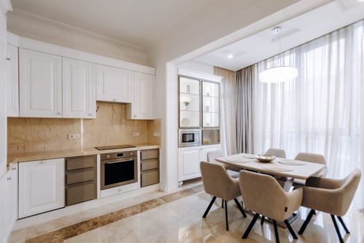 In a lovely house, there exists a kitchen and a dining room that features a wellset table accompanied by several comfortable chairs